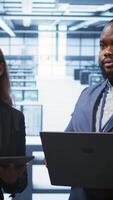 Vertical Teamworking colleagues doing checkup, inputting data on laptop of needed server hub fixes. Coworkers working together in data center housing advanced storage infrastructure, camera B video