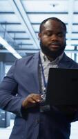 Vertical IT engineer working on laptop in modern data center, overseeing server operations, system maintenance,and cybersecurity protocols, ensuring optimal performance and data integrity, camera A video