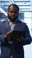 Vertical Software developer managing data center with advanced technology, ensuring efficient network management. Admin walking in server room, optimizing data center infrastructure with tablet, camera A video