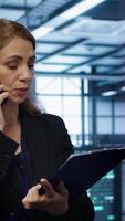 vertikal den specialist ser över data Centrum underhåll checklista, talande på telefon i server odla. anställd omgiven förbi server kuggstänger talande under telefon ringa upp, kamera en video