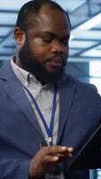 Vertical IT technician walking in data center, overseeing server operations using tablet. Expert ensuring optimal performance and data integrity in server hub using digital device, camera A video