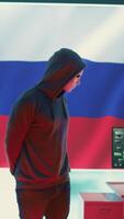 Vertical Russian hacker in a governmental IT environment with a russian flag on big screen, dealing with cyber terror, ransomware and espionage. Installing misinformation and aggression propaganda. Camera B. video