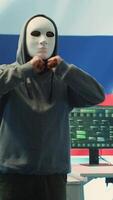 vertical anônimo pessoa com mascarar pergunta para resgate dentro russo governamental hacking quarto com a nacional bandeira. lidando com cyber espionagem, desinformação campanhas e híbrido guerra propaganda. Câmera uma. video