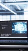 Vertical Laptop in data center facility with artificial intelligence computing simulating human brain, handheld camera shot. Close up of device displaying AI machine learning algorithms in server hub, camera B video