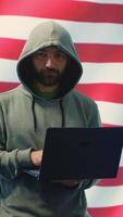 Vertical A hacker working in a governmental IT workspace with the USA flag running on big screen. Ensuring cybersecurity, cyber threat analysis and global surveillance to ensure cyber protection. Camera A. video