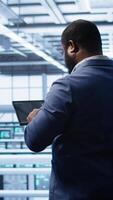 Vertical Computer scientist in data center running error checking utilities on tablet to fix bugs. IT expert in server hub facility looking for network issues affecting supercomputers performance, camera B video