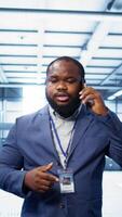 Vertical IT technician talking on phone in data center, coordinating server maintenance and troubleshooting tasks. Manager surrounded by server racks and high tech equipment in telephone call, camera B video