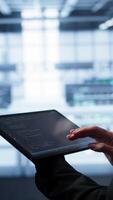 Vertical System administrator doing annual checkup using tablet to prolong data center equipment life span. Close up shot of IT expert in server hub monitoring supercomputers using digital device, camera B video