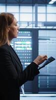 Vertical Technician doing checkup using tablet to prolong data center electronics life span and avoid downtime. Employee walking in server room, monitoring server infrastructure using digital device, camera B video