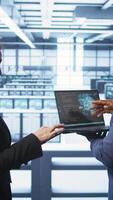 Vertical Teamworking coworkers doing maintenance using devices, prolonging data center hardware life span. Colleagues doing brainstorming in server hub, monitoring server infrastructure using devices, camera B video