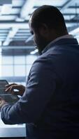Vertical Technician in server hub workplace installing newly ordered storage unit, checking parameters with tablet. IT expert in data center holding device, replacing storage mainframes components, camera B video