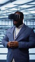 Vertical African american developer immersed in virtual reality at data center, doing units maintenance. Technician using VR headset to optimize servers performance, checking operations, camera B video