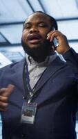 Vertical IT support worker in data center talking in phone call, doing yearly checkup. On field engineer chatting with manager in server hub during telephone call, monitoring servers infrastructure, camera A video