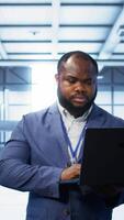 Vertical Computer scientist in data center using diagnostic tools and system monitoring software on laptop to identify cause of errors. IT specialist in server farm establishment repairing equipment, camera B video