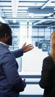 Vertical Data center engineer presenting equipment to inspector supervising operations. IT specialist in server farm doing tour for supervisor monitoring equipment performance, camera B video