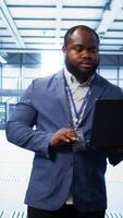 Vertical IT engineer working on laptop in modern data center, overseeing server operations, system maintenance,and cybersecurity protocols, ensuring optimal performance and data integrity, camera B video