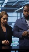 Vertical System administrators looking at holograms in data center, doing swiping motions hand gestures. Server farm workplace employees interacting with augmented reality tech, camera A video