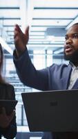 Vertical System administrators in data center overseeing server operations using notebook and tablet. Colleagues brainstorming in server hub, ensuring optimal performance and data integrity, camera B video
