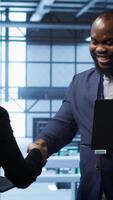 Vertical African american admin greeting inspector arriving in data center to supervise operations. IT expert in server hub workspace doing hand shake with supervisor monitoring performance, camera A video