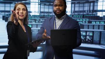 Teamworking colleagues doing checkup, inputting data on laptop of needed server hub fixes. Coworkers working together in data center housing advanced storage infrastructure, camera A video