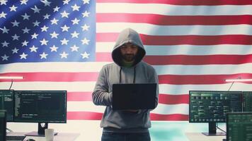 A hacker working in a governmental IT workspace with the USA flag running on big screen. Ensuring cybersecurity, cyber threat analysis and global surveillance to ensure cyber protection. Camera B. video