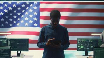 Cybersecurity expert working in a governmental hacking room with the American flag shown on big screen. Safeguarding data protection and doing cyber threat analysis in a high tech office. Camera B. video