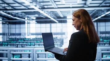 Computer scientist doing yearly maintenance using laptop to prolong data center equipment life span. IT specialist in server hub facility monitoring server infrastructure using device, camera B video