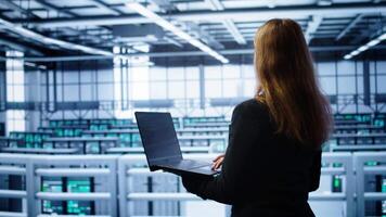 System administrator in server farm using laptop to patch network issues leading to slow data transfer rates. IT support staff member in data center fixing errors affecting supercomputers, camera B video