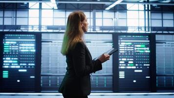 Engineer in server hub checking recovery plan on tablet, monitoring rackmounts energy consumption. Woman in data center making sure rigs are functioning optimally, doing routine disk checks, camera B video