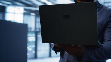 Technician in server hub using laptop to patch network issues leading to slow data transfer rates. Close up of IT professional in data center fixing errors affecting supercomputers, camera B video