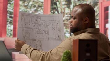 Corporate owner planning an office interior design renovation, reviewing blueprints and collaborating with contractors to create a modern workspace. Evaluating property sketches at home. Camera A. video