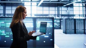 Woman walking in high tech facility, using laptop to patch network issues leading to slow data transfer rates. Employee in data center fixing errors affecting servers performance, camera B video