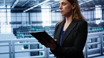 Admin in server room checks recovery plan on tablet, monitoring equipment energy consumption. IT professional uses notebook in data center workplace, ensuring rigs are functioning optimally, camera B video