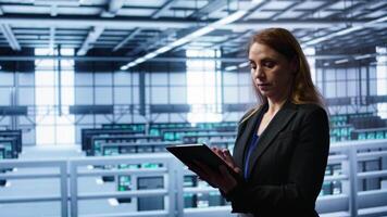 Meticulous technician doing checkup, inputting data on tablet of needed fixes in server hub housing advanced data storage infrastructure supporting critical IT workloads, camera B video