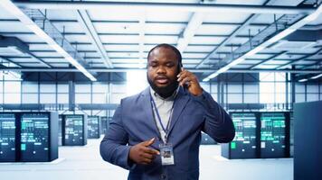 IT technician talking on phone in data center, coordinating server maintenance and troubleshooting tasks. Manager surrounded by server racks and high tech equipment in telephone call, camera B video
