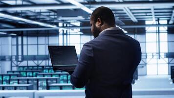 Computer scientist in server farm using laptop to patch network issues leading to slow data transfer rates. IT expert in data center establishment fixing errors affecting supercomputers, camera A video
