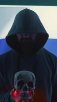 Vertical Conceptual image of a hooded russian hacker creating hazardous alerts, holds a skull and warning of death threats. Russian federation works on cybercrime and violence, panic and torment. Camera B. video