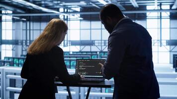 Team of developers doing maintenance checkup using laptop to prolong data center hardware life span. IT support staff members in server hub monitor server infrastructure using notebook, camera A video