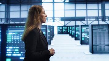 Engineer walking in data center workspace, monitoring systems to identify root cause of errors. Woman in server hub establishment doing diagnosis, looking for equipment bugs needing repairs, camera A video