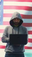 Vertical A hacker working in a governmental IT workspace with the USA flag running on big screen. Ensuring cybersecurity, cyber threat analysis and global surveillance to ensure cyber protection. Camera B. video