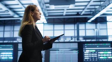 Engineer in server hub checking recovery plan on tablet, monitoring rackmounts energy consumption. Woman in data center making sure rigs are functioning optimally, doing routine disk checks, camera A video