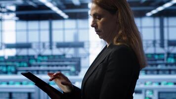 Meticulous technician doing checkup, inputting data on tablet of needed fixes in server hub housing advanced data storage infrastructure supporting critical IT workloads, camera A video