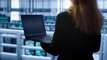 System administrator in server farm using laptop to patch network issues leading to slow data transfer rates. IT support staff member in data center fixing errors affecting supercomputers, camera A video