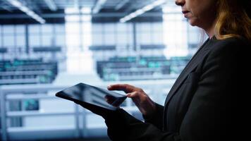 System administrator monitoring server room, doing checkup, inputting data on tablet of needed fixes. IT support employee working in data center facility housing storage rackmounts, camera B close up video