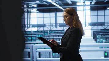 Computer scientist doing checkup, inputting data on tablet of needed fixes in server hub. Woman working in data center housing advanced data storage infrastructure supporting IT workloads, camera A video