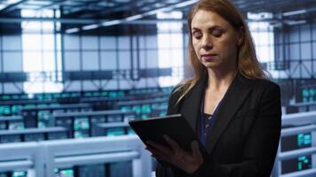 Admin in server room checks recovery plan on tablet, monitoring equipment energy consumption. IT professional uses notebook in data center workplace, ensuring rigs are functioning optimally, camera A video