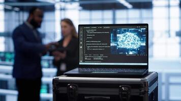 Focus on laptop in data center with artificial intelligence brain used by engineers in blurry background. Close up of device displaying AI deep learning software in server farm, camera A video