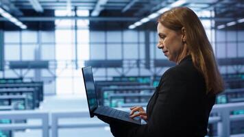 Computer scientist doing yearly maintenance using laptop to prolong data center equipment life span. IT specialist in server hub facility monitoring server infrastructure using device, camera A video