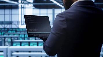 Programmer doing yearly maintenance checkup using laptop to prolong data center electronics life span. IT professional in server farm monitoring server infrastructure using notebook, camera A video