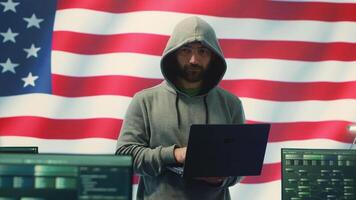 A hacker working in a governmental IT workspace with the USA flag running on big screen. Ensuring cybersecurity, cyber threat analysis and global surveillance to ensure cyber protection. Camera A. video